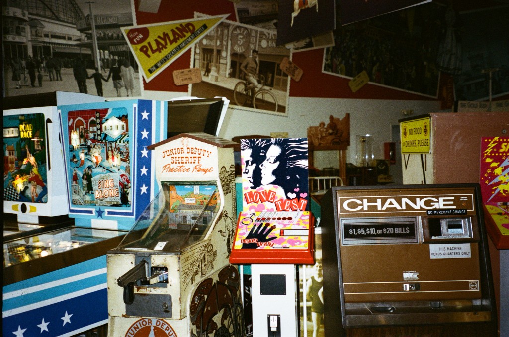 Vintage arcade cabinets including a Junior Deputy Sheriff shooting game, Love Test machine, and a bill-to-quarters change machine, with Playland memorabilia on the wall